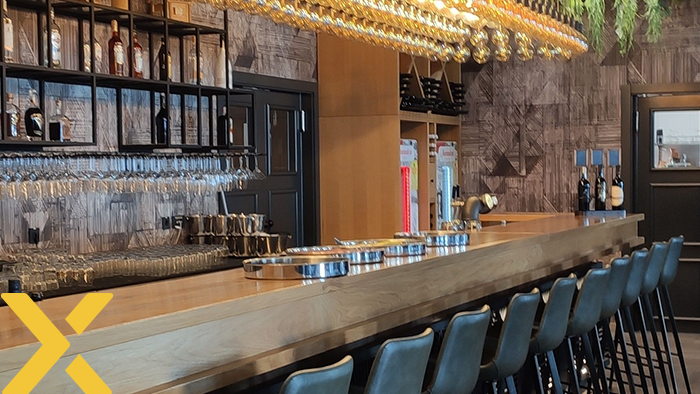 Sfeervolle barinterieur met houten bar, een rij barkrukken, glazen en flessen achter de bar en sfeerverlichting aan het plafond