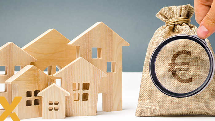 Houten huisjes naast een geldzak met euroteken onder een vergrootglas.