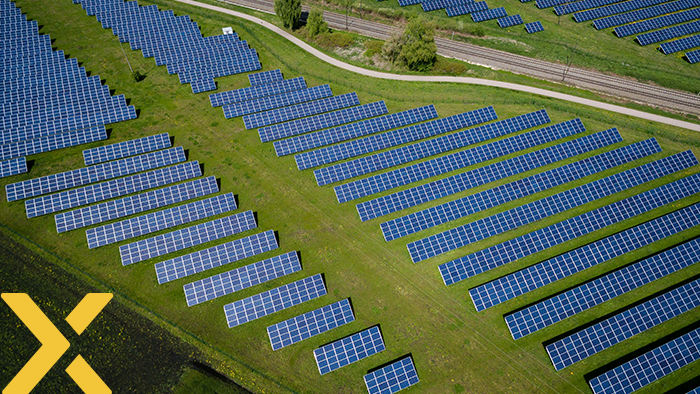Luchtfoto van een groot zonnepark met rijen zonnepanelen, omgeven door grasland