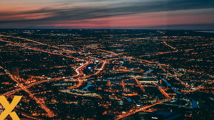 Luchtfoto van een uitgestrekte stad bij avond met verlichte wegen en gebouwen, symbool voor energieverbruik en netbelasting.