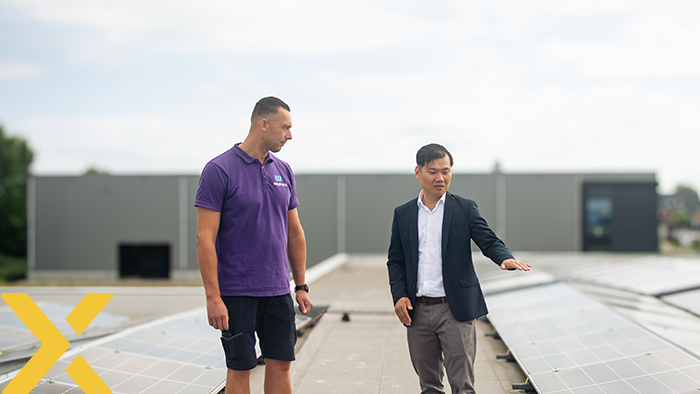 Twee personen staan tussen rijen zonnepanelen op een plat dak, terwijl zij iets over de zonnepanelen bespreken