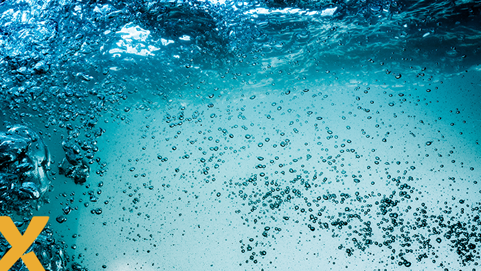 Onderwaterbeeld van helder blauw water met talloze opstijgende luchtbellen en een golvend wateroppervlak