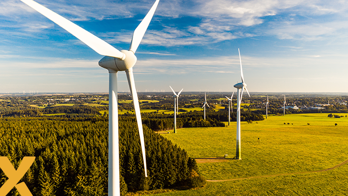 Luchtfoto van een windmolenpark met meerdere windturbines verspreid over groene velden en bosgebied onder een heldere blauwe hemel