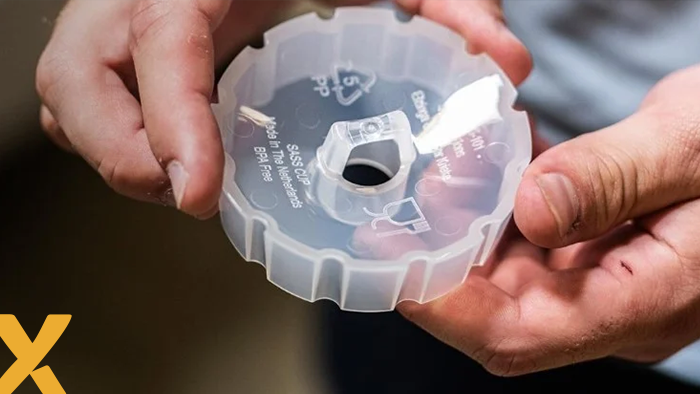 Persoon houdt een kunststof onderdeel vast met recycling- en materiaalinformatie erop gedrukt.