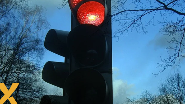 Verkeerslicht met rood licht aan tegen een blauwe hemel en silhouet van boomtakken.