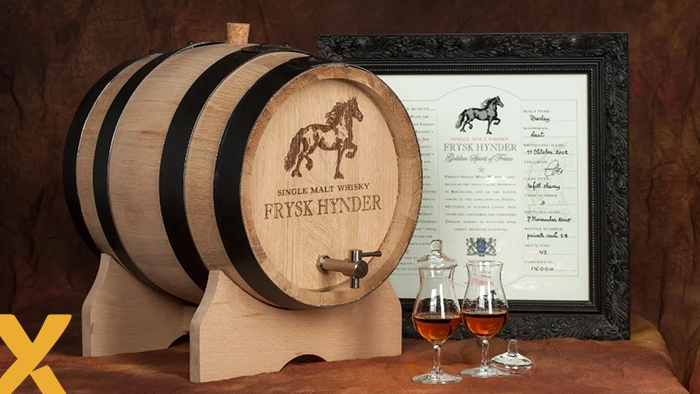 Een houten whiskyvat met het logo van ‘Frysk Hynder’ en twee gevulde whiskyglazen op de voorgrond, naast een ingelijste certificaat.
