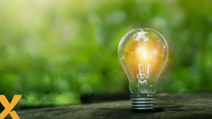 Brandende gloeilamp op een houten oppervlak met groene, natuurlijke achtergrond – symbool voor duurzame energie.