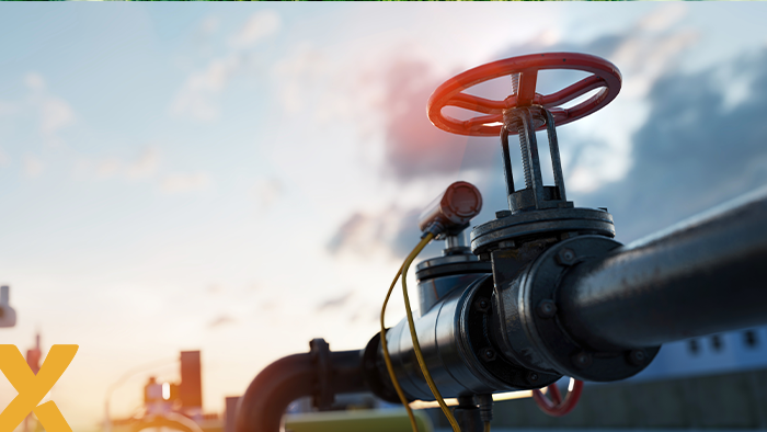 Gaspijpleiding met rode afsluiter en drukmeter in een industriële omgeving bij zonsopkomst, symbool voor gasvoorziening en energieprijzen.