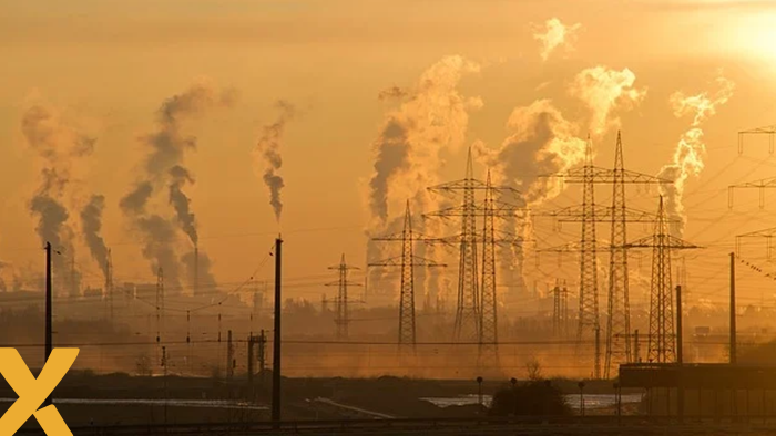 Industriële omgeving met rokende schoorstenen en hoogspanningsmasten bij zonsopgang.