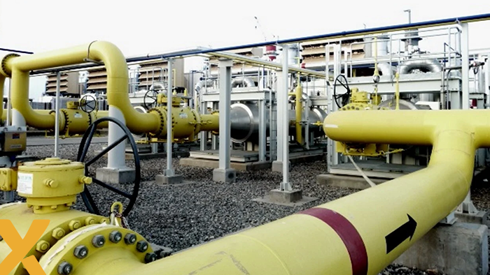 Industriële installatie met gele gaspijpen, kleppen en drukregelaars op een grindbodem in een gasverdelingsstation.