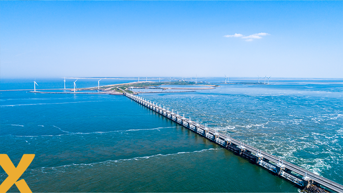 Luchtfoto van de Oosterscheldekering met windmolens op de achtergrond, symbool voor duurzame energie in Zeeland.