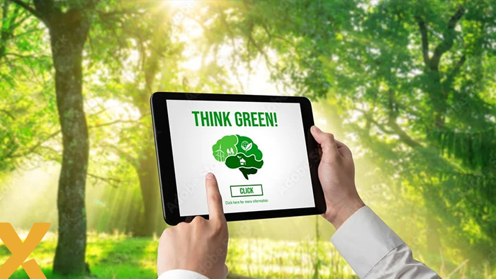 Persoon houdt tablet vast met de tekst 'Think Green!' op het scherm, in een zonnig bos als achtergrond.