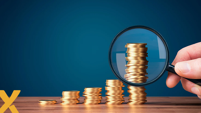 Stapelende munten onder een vergrootglas op een houten tafel, symbool voor financiële groei en analyse.