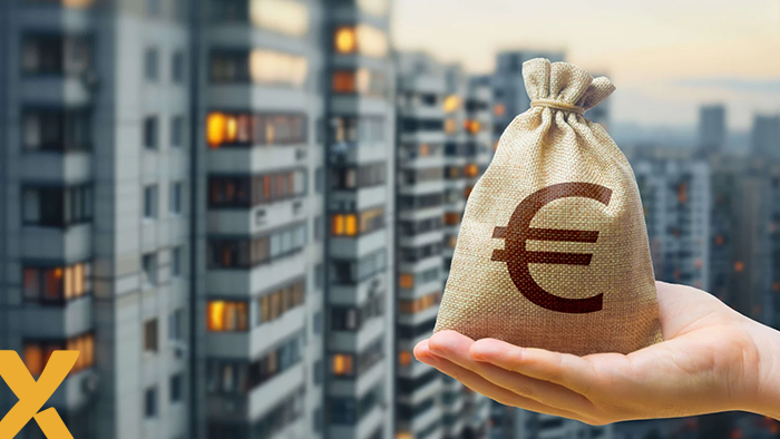 Hand met een zak geld voorzien van euroteken, met op de achtergrond een appartementencomplex in de stad.