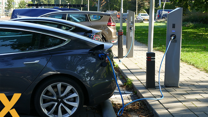 Elektrische auto's opgeladen bij publieke laadpalen op een parkeerplaats in een groene stedelijke omgeving.