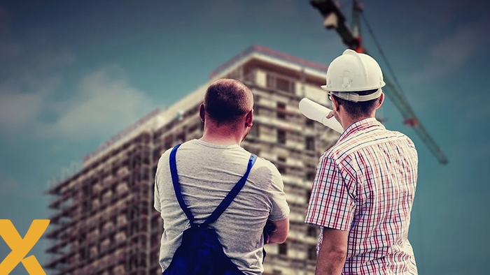 Twee bouwvakkers bekijken een in aanbouw zijnd appartementencomplex met een hijskraan op de achtergrond.