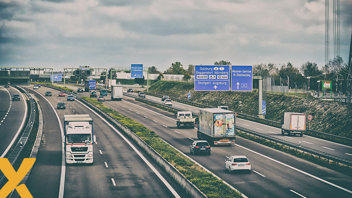 Drukke snelweg met vrachtwagens en auto's onder een bewolkte hemel, met borden richting Duitse steden zoals Salzburg en Stuttgart.