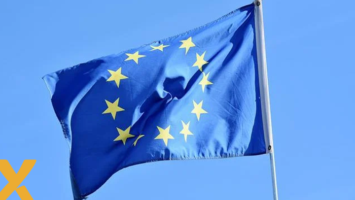 Europese vlag met twaalf gele sterren op blauwe achtergrond, wapperend tegen een heldere hemel.