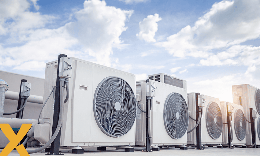 Een rij witte airconditioningunits op een dak, met een blauwe lucht en wolken op de achtergrond.