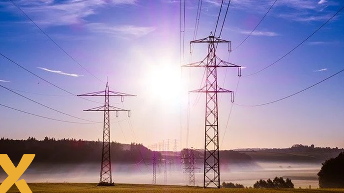 Hoogspanningsmasten in een mistig landschap bij zonsopgang, met elektriciteitskabels die over groene velden lopen.