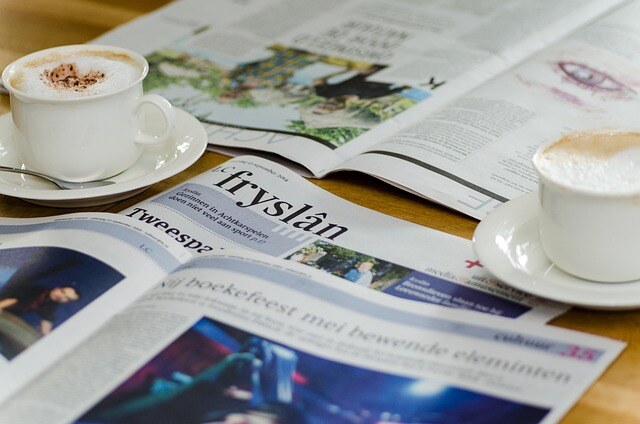 Twee kopjes cappuccino op een tafel met verschillende opengeslagen kranten, waaronder de Friese krant 'Fryslân'.