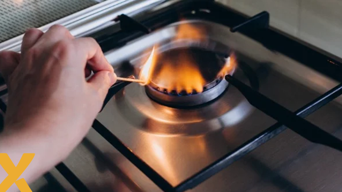 Hand die een gasfornuis aansteekt met een lucifer, vlam zichtbaar op de brander.