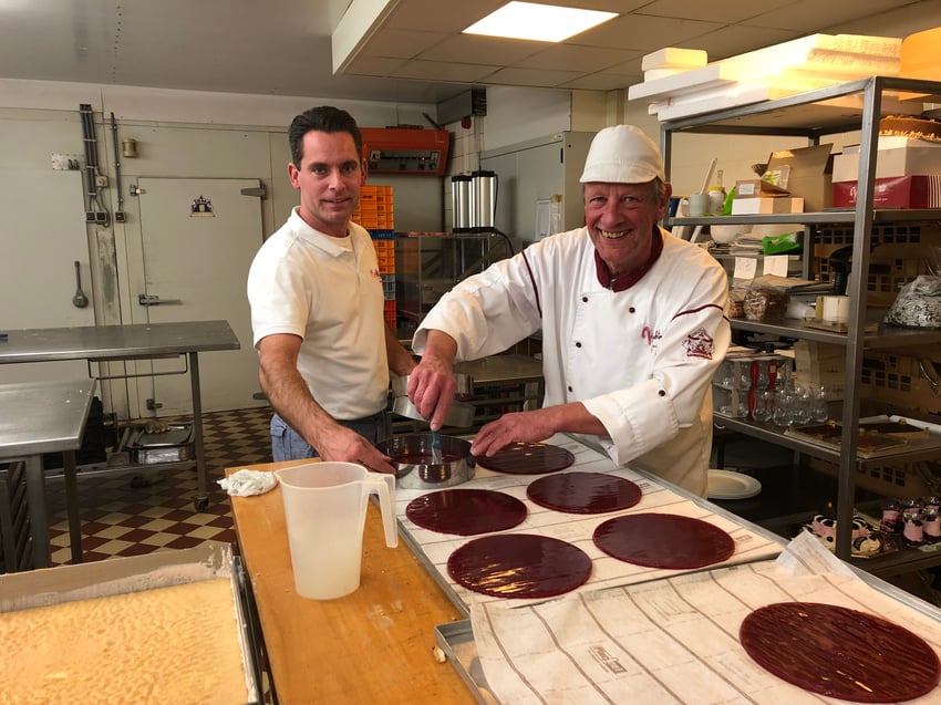 Twee bakkers in banketbakkerij Mekking die samen lachend chocolade glazuur op taarten aanbrengen.