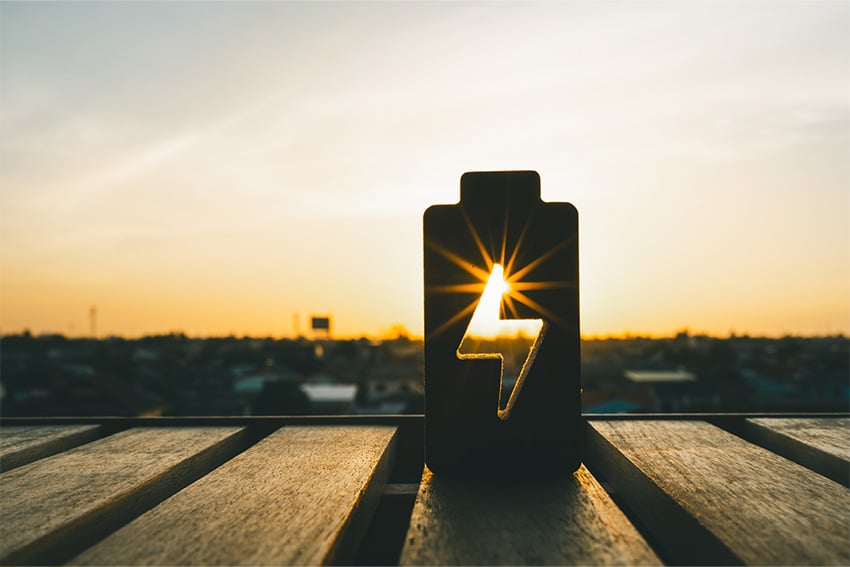 Silhouet van een batterijvormig object met een bliksemsymbool, verlicht door de ondergaande zon op de achtergrond, als symbool voor duurzamen energieopslag.