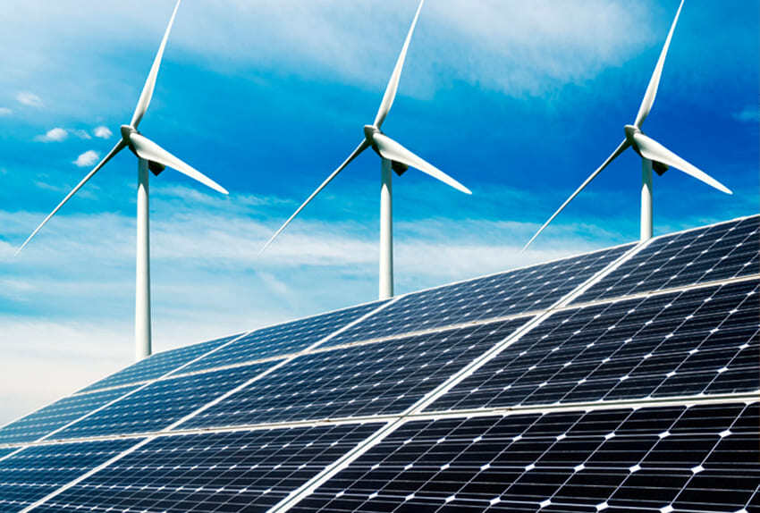 Zonnepanelen op de voorgrond met daarachter drie draaiende windturbines onder een heldere blauwe lucht, als symbool voor duurzame energiebronnen.