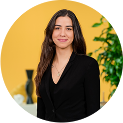 Professionele portretfoto van een glimlachende vrouw met lang donker haar, gekleed in een zwarte blazer, voor een gele achtergrond met een plant en moderne decoratie. Professionele portretfoto van een glimlachende vrouw met lang donker haar, gekleed in een zwarte blazer, voor een gele achtergrond met een plant en moderne decoratie.